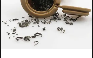 Primo piano dell'infusore per tè in silicone marrone a forma di cacca con foglie di tè sfuse