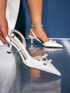 Elegant detail of white pointed-toe heels with double bows and ankle strap for women