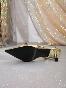 Detailed view of the black non-slip sole and glittery kitten heel of gold slingback shoes