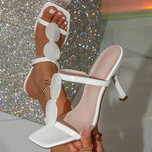 Primo piano di sandali bianchi con tacco alto e decorazioni ovali per la moda estiva.
