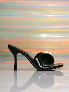 Dettaglio laterale di un elegante sabot nero con tacco alto e grande perla
