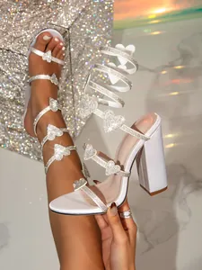 Detail von weißen Blockabsatz-Sandalen mit Strass-Herz-Akzenten und Wickelriemen-Design