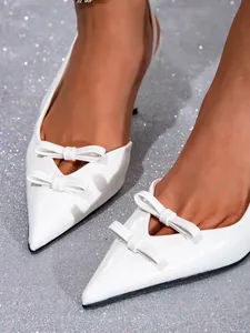 Close-up of white pointed-toe slingback pumps with elegant double bow detail.