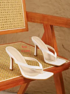 Detail van witte stiletto teensandalen met een hak van 9 cm op een rotan stoel
