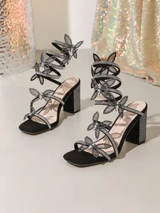 Détail de sandales noires à lanières serpent, nœuds papillon strass et talon bloc