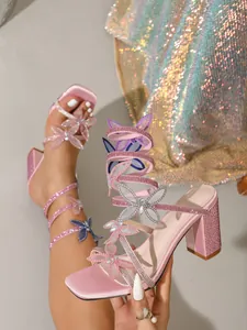 Gros plan de sandales roses à brides papillon en strass et talons blocs
