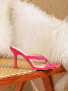 Elegante roze thong sandalen met hoge hak gepresenteerd op een stijlvolle rieten stoel