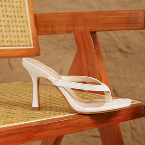 Elegante witte Franse stijl teensandalen met hoge hak op een houten rotan stoel.