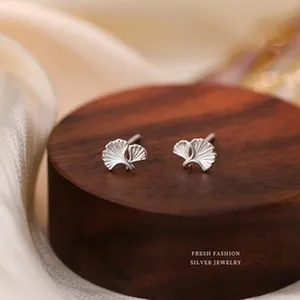 Close-up view of S925 sterling silver ginkgo leaf stud earrings on a dark wood stand