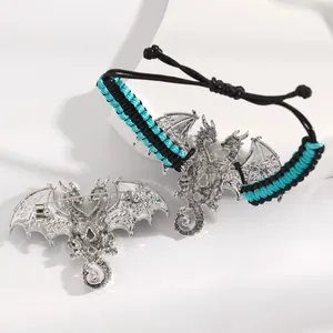 Detailed view of a silver dragon brooch and matching black-cyan woven cord bracelet.