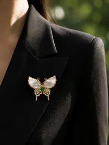 Detailed shot of a luxury butterfly brooch with shell wings and green gem on a black blazer.