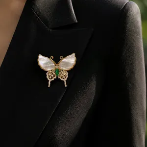 Elegant gold butterfly brooch featuring white shell wings and green emerald gemstone