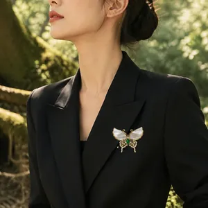 Elegant butterfly brooch with white shell wings and emerald stone on a black blazer