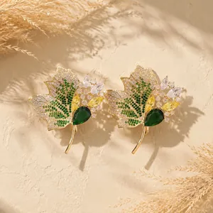 Nahaufnahme von eleganten goldenen Ahornblatt-Broschen mit grünen und gelben Kristallen.