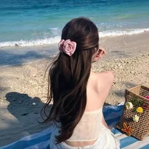 Μοντέλο από πίσω που φοράει ροζ υφασμάτινο κλιπ μαλλιών τριαντάφυλλο στην παραλία