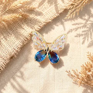 Dettaglio macro di un'elegante spilla a farfalla dorata con cristalli blu luccicanti.