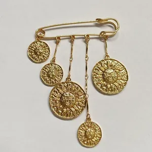 Nahaufnahme goldene Sicherheitsnadel-Brosche mit Sonnen-Münzanhängern im Punk-Stil.