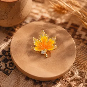 Close-up of a vintage maple leaf brooch with orange enamel and a small clear gemstone.