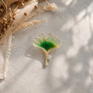 Macro view of an elegant golden ginkgo leaf brooch with green resin and a clear crystal.