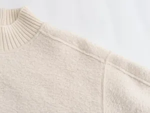Macro view of the textured bouclé fabric and ribbed collar on a cream white sweater