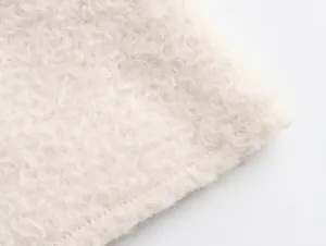 Macro detail shot of soft white curly faux fur fabric texture showing a stitched edge