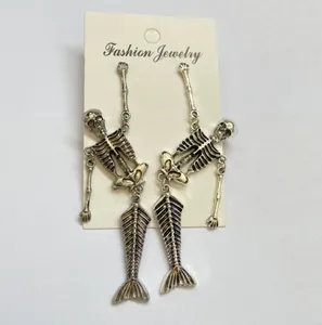 Detailed view of gothic skeleton mermaid dangling earrings on a white jewelry card