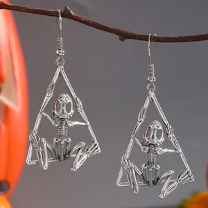 Detail view of gothic skeleton earrings in a triangle frame hanging on a dark branch.