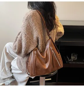 Vue détaillée d'un grand sac à bandoulière en cuir marron porté sur un pull en maille.