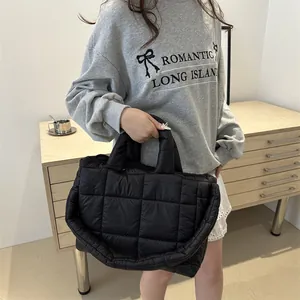 Primer plano de un bolso acolchado negro sostenido por una modelo en un ambiente casual