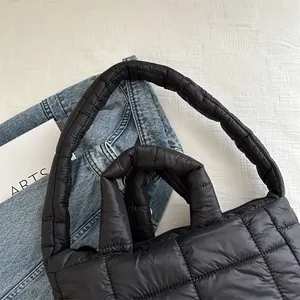 Detalle del bolso de hombro acolchado negro con textura suave y asas acolchadas.