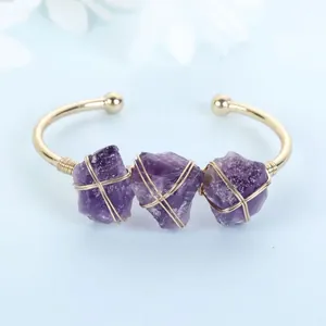Close-up detail of three purple raw amethyst stones wire-wrapped on a gold open bangle