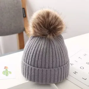 Detailansicht einer grauen Strickmütze für Kinder mit braunem Kunstfellbommel.