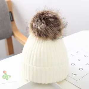 Nahaufnahme einer weißen Strickmütze für Babys mit einem großen flauschigen braunen Bommel