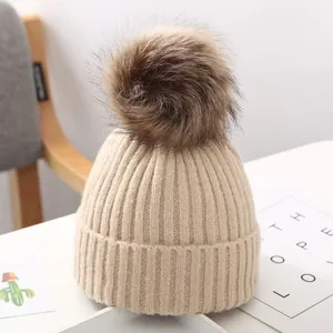 Nahaufnahme einer warmen beigen Strickmütze mit flauschigem Kunstfellbommel für Kinder.