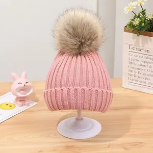 Detailansicht einer rosa gestrickten Babymütze mit einem großen, flauschigen Kunstfellbommel