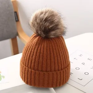 Detaillierte Nahaufnahme einer caramel Strickmütze für Kinder mit einem großen Kunstfellbommel.