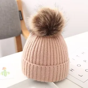 Detailansicht einer rosa gestrickten Babymütze mit flauschigem braunem Kunstfellbommel