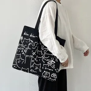 Bolso tote grande de lona negra con estampado de gato blanco llevado por modelo