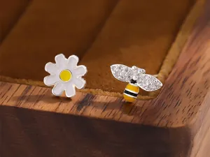 Gros plan de boucles d'oreilles asymétriques abeille et marguerite avec cristaux