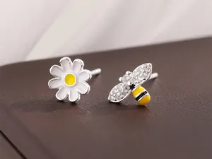 Gros plan de boucles d'oreilles asymétriques en argent avec marguerite et abeille brillante.