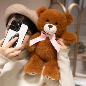 Adorable brown teddy bear plush toy with a pink polka dot bow tie held in a cozy scene