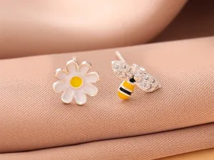 Détail de boucles d'oreilles asymétriques marguerite et abeille en cristal sur tissu.