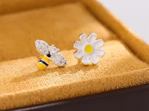Gros plan de boucles d'oreilles asymétriques abeille et marguerite avec cristaux brillants