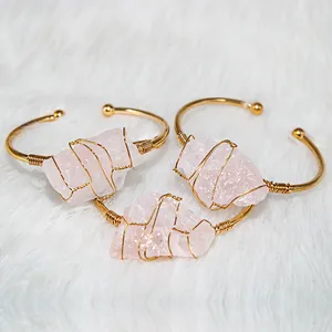 Detail of handmade rose quartz wire-wrapped gold adjustable bangles on white fur.