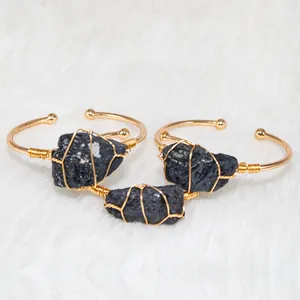 Detail of hand-wrapped gold cuffs with irregular black natural stones on white fur.