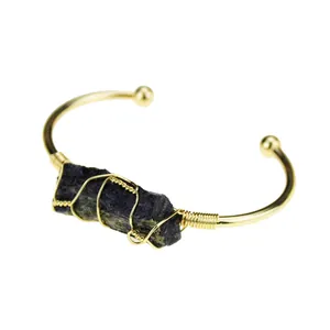 Detail view of the wire-wrapped irregular dark crystal on a gold-plated open cuff bangle