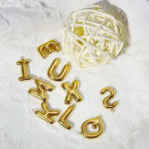Close-up of 18k gold plated puffy balloon alphabet charms on white knitted texture.