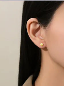 Nahaufnahme eines minimalistischen kleinen goldenen Bohnen-Ohrsteckers am weiblichen Ohr