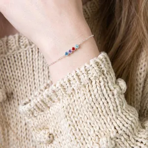 Gros plan d'un bracelet en argent minimaliste avec quatre pierres de naissance.