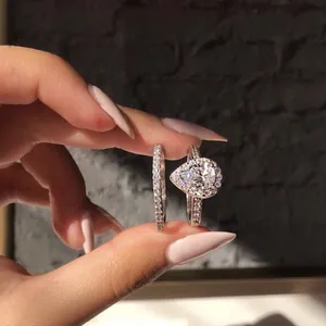 Exquisite pear-shaped halo engagement ring and pavé eternity band set held by hand